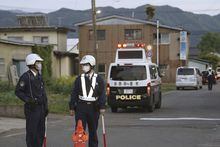 Police officers stand guard on a street leading to a building where a man is holed up in Nakano, central Japan, Thursday, May 25, 2023. A masked man carrying a rifle and a knife was holed up in a building Thursday in Nagano, a city of Nagano prefecture. Multiple people were injured, one of whom later died, police said. (Kyodo News via AP)