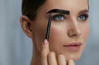 Eyebrow coloring. Woman applying brow tint with makeup brush closeup. Girl model using liquid peel-off brow gel, beauty product on eyebrows
