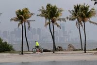 The Miami skyline is shrouded in clouds as a cyclist rides along Biscayne Bay at Matheson Hammock Park, Friday, May 15, 2020, in Miami. A trough of low pressure moving through the Florida Straits could organize over the northwest Bahamas later Friday or Saturday and become the first named storm of the 2020 hurricane season, the U.S. National Hurricane Center in Miami said. (AP Photo/Lynne Sladky)