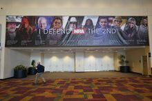 A guest walks under a sign advertising the NRA Convention, Thursday, April 13, 2023, in Indianapolis. The convention starts Friday, April 14 and end on Sunday, April 16. (AP Photo/Darron Cummings)