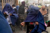 A Taliban fighter walks among people waiting to receive food rations distributed by a South Korea humanitarian aid group, in Kabul, Afghanistan, Tuesday, May 10, 2022. (AP Photo/Ebrahim Noroozi)