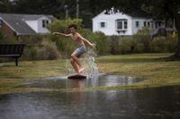 Zach Wright, 12, skimboards in floodwaters from the Lafayette River in the Larchmont Neighborhood of Norfolk, Va., Friday, Sept. 22, 2023, as Tropical Storm Ophelia approaches. (Kendall Warner/The Virginian-Pilot via AP)