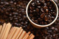 A top view image of dark roasted coffee beans and wooden stir sticks.