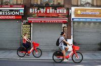 Two cyclists are seen passing closed souvenir shops, in London, on May 7, 2020.