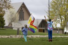 John and Sarah Barbier wave at vehicles while holding a Pride flag across the road from the Netherlands Reformed Congregation church in Norwich, Ont., on Wednesday, May 3, 2023. The southern Ontario township voted last month to prohibit Pride flags on municipal property. THE CANADIAN PRESS/Nicole Osborne