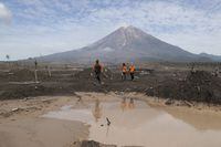 Rescuers walk on an area affected by the eruption of Mount Semeru, background, during a search for victims in Lumajang, East Java, Indonesia, Wednesday, Dec. 8, 2021. Heavy rains and torrents of hot lava and mud sliding down the erupting volcano Java island have put search and rescue operations for more than a dozen missing on hold, officials said Wednesday. (AP Photo/Trisnadi)