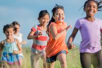 A multi-ethnic group of elementary age children are running through a grassy field and are playing tag outside on a warm sunny day. children running exercise kids fitness