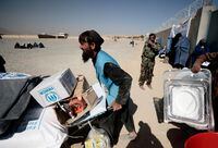 FILE PHOTO: An UNHCR worker pushes a wheelbarrow loaded with aid supplies for a displaced Afghan family outside a distribution center as a Taliban fighter secures the area on the outskirts of Kabul, Afghanistan October 28, 2021. REUTERS/Zohra Bensemra/File Photo