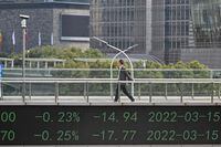 People walk across a bridge with a stocks indicator board in the financial district of Shanghai on March 16, 2022. (Photo by Hector RETAMAL / AFP) (Photo by HECTOR RETAMAL/AFP via Getty Images)
