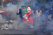 Supporters of former Prime Minister Imran Khan take cover after riot police officers fire tear gas to disperse them during clashes, in Lahore, Pakistan, Wednesday, March 15, 2023. Supporters of Khan threw bricks at police who fought back with clubs and tear gas for a second day Wednesday after officers tried to arrest the ousted premier for failing to appear in court on graft charges.(AP Photo/K.M. Chaudary)