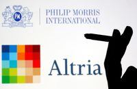 A hand with a cigarette is seen in front of displayed logos of Philip Morris and Altria in this picture illustration taken September 26, 2019. REUTERS/Dado Ruvic/Illustration/Files