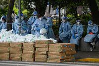 Workers stand next to boxes of food to be delivered in a neighborhood during a Covid-19 coronavirus lockdown in the Jing'an district in Shanghai on May 7, 2022. (Photo by Hector RETAMAL / AFP) (Photo by HECTOR RETAMAL/AFP via Getty Images)