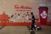 FILE PHOTO: A man walks past a store front poster advertising the opening of a cafe of the Canadian coffee and fast food chain Tim Hortons in Beijing, China, July 6, 2020. REUTERS/Thomas Peter/File Photo