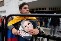 A supporter holds photos of presidential candidate Gustavo Petro, with the Historical Pact coalition, outside the polling station where he voted in a presidential runoff in Bogota, Colombia, Sunday, June 19, 2022. (AP Photo/Fernando Vergara)
