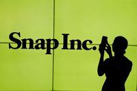 A woman stands in front of the logo of Snap Inc. on the floor of the New York Stock Exchange (NYSE) while waiting for Snap Inc. to post their IPO, in New York City on March 2, 2017.