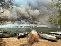 Boats are pulled ashore as smoke and wildfires rage behind Lake Conjola, Australia, on Jan. 2, 2020.