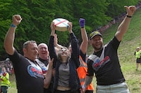 Delaney Irving holds the cheese after winning the women's downhill race during the Cheese Rolling contest at Cooper's Hill in Brockworth, Gloucestershire, Monday May 29, 2023. The Cooper's Hill Cheese-Rolling and Wake is an annual event where participants race down the 200-yard (180 m) long hill chasing a wheel of double gloucester cheese. (AP Photo/Kin Cheung)