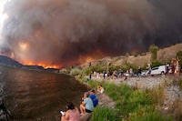 (FILES) Residents watch the McDougall Creek wildfire in West Kelowna, British Columbia, Canada, on August 17, 2023, from Kelowna. Ottawa estimates the annual cost of fighting wildfires at Can$1 billion, and noted that, according to the Canadian Climate Institute, climate impacts such as more and bigger fires could halve Canada's projected economic growth in the coming years. Most worrying, he said, is that Canadians aren't dealing anymore with one localized disaster every few years or decades, but rather "several events stacked on top of each other in a single year" -- including fires, floods, heatwaves and powerful storms. (Photo by Darren HULL / AFP) (Photo by DARREN HULL/AFP via Getty Images)