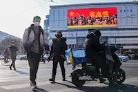 People walk across a street near a large screen promoting the Chinese People's Liberation Army carrying the words "Bloody" outside a mall in Beijing, Monday, Jan. 9, 2023. The Chinese military held large-scale joint combat strike drills starting Sunday, sending war planes and navy vessels toward Taiwan, both the Chinese and Taiwanese defense ministries said. (AP Photo/Andy Wong)
