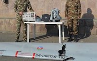 Two soldiers at an Armenian military compound pose with a wing of a downed Turkish-made Bayraktar TB2 drone and the Canadian-made L3 Harris Wescam airstrike targeting gear. Armenia says all the parts were on a drone captured in the Nagorno-Karabakh conflict. One soldier is holding the October 29, 2020 front page of the Hayastani Hanrapetutiun newspaper. Date of photo is October 29, 2020. Photo credit: Neil Hauer.