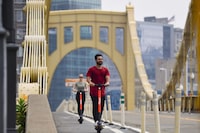 Ka'ai Tom, of Oahu, Hawaii, and Brittany Janicki, from the Brooklyn borough of New York, cross the Roberto Clemente Bridge in Pittsburgh on SPIN scooters, Tuesday, July 20, 2021. (Jack Myer/Pittsburgh Post-Gazette via AP)