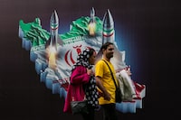 People in Tehran on Thursday, April 18, 2024, walk past a mural depicting Iranian missiles. Israel struck Iran early Friday, April 19, 2024, according to officials from both countries, in what appeared to be its first military response to the Iranian attack on Israel last weekend.  (Arash Khamooshi/The New York Times)