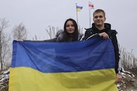 In this photo provided by the Ukrainian Presidential Press Office, Ukrainian teenager Bohdan Yermokhin, right, holds the Ukraine flag on the Ukraine-Belarus border in Ukraine, Sunday, Nov. 19, 2023. The orphaned Ukrainian teenager was taken to Russia last year during the war in his country and has now returned home after being reunited with relatives in Belarus on his 18th birthday Sunday. (Ukrainian Presidential Press Office via AP)