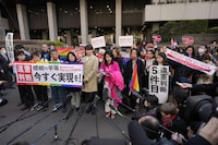 A lawyer, in pink clothes, center, for the plaintiffs standing to her right speaks in front of media members by the main entrance of the Tokyo district court after hearing the ruling regarding LGBTQ+ marriage rights, in Tokyo, Thursday, March 14, 2024. The Japanese court on Thursday ruled that not allowing same-sex couples the same marital benefits as heterosexuals violates their fundamental right to have a family, but the current civil law did not take into consideration sexual diversity and is not clearly unconstitutional, a partial victory for Japan's LGBTQ+ community calling for equal marriage rights. (AP Photo/Hiro Komae)