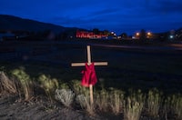 A child's dress is seen on a cross outside a former residential school in Kamloops, B.C., Sunday, June 13, 2021. An interim report from an international group hired to provide advice on identifying and locating the unmarked graves of children who attended residential schools says Canada can should continue funding searches beyond 2025. THE CANADIAN PRESS/Jonathan Hayward