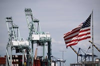 (FILES) The US flag blows in the wind as cranes stand above cargo shipping containers on ships at the Port of Los Angeles in Los Angeles, California on June 7, 2023. The US trade deficit expanded in September on the back of a larger rise in imports than exports, according to government data released on November 7, 2023. The overall trade gap of the world's biggest economy broadened more than expected to $61.5 billion, up from a revised $58.7 billion in August, said the Commerce Department. (Photo by Patrick T. Fallon / AFP) (Photo by PATRICK T. FALLON/AFP via Getty Images)