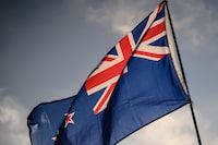 A man raises a New Zealand flag as he attends a vigil in memory of the twin mosque massacre victims in Christchurch on March 24, 2019. - New Zealand will hold a national remembrance service for victims of the Christchurch massacre on March 29, the government announced, as the country grieves over a tragedy that shocked the world. (Photo by Anthony WALLACE / AFP)ANTHONY WALLACE/AFP/Getty Images