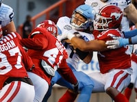 Toronto Argonauts quarterback Cameron Dukes, centre, is sacked by Calgary Stampeders defensive lineman Isaac Adeyemi-Berglund, right, during second half CFL football action in Calgary, Friday, Aug. 4, 2023.THE CANADIAN PRESS/Jeff McIntosh