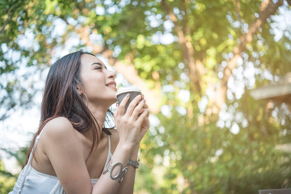 Young beautiful woman feeling happy and powerful while drinking coffee at the park in the morning
