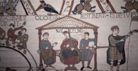 A combo shows a picture of a scene of the queen from the television series "Game of Thrones" in a 87 meters tapestry relating the 8 seasons of the US (top) and a part of the the "Bayeux tapestry" or "Queen Mathilde tapestry" which relate Britain's conquest by William the Conqueror (Guillaume le Conquerant) in 1066 on September 13, 2019 in Bayeux. - Like the Bayeux Tapestry, the Game of Thrones Tapestry is woven of fine linen and hand-embroidered, with decorative borders and a central pictorial narrative. (Photo by LOIC VENANCE / AFP)        (Photo credit should read LOIC VENANCE/AFP via Getty Images)
