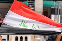 A demonstrator holds a copy of the Koran, Islam's holy book, while another holds an Iraqi national flag during the weekly Friday prayers at the Grand Mosque of Kufa in Iraq's central shrine city of Kufa east of nearby Najaf on July 21, 2023 as they denounce the burning of the Koran in Sweden. (Photo by Qassem al-KAABI / AFP) (Photo by QASSEM AL-KAABI/AFP via Getty Images)