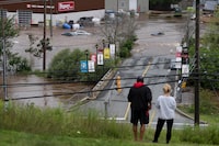 People stand on a hill surveying cars abandoned in floodwater in a mall parking lot following a major rain event in Halifax on Saturday, July 22, 2023. THE CANADIAN PRESS/Darren Calabrese