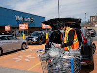 A Walmart employee loads groceries into a vehicle parked in a dedicated customer pick up spot at the Walmart by the Dufferin Mall, on April 5 2020.
