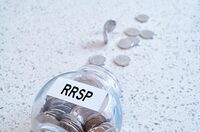 Glass jar with many coins and RRSP word over a marble counter top.Canadian Registered Retirement Savings fund concept.
