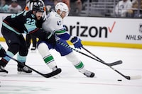 Seattle Kraken right wing Oliver Bjorkstrand (22) and Vancouver Canucks defenseman Noah Juulsen (47) battle for the puck during the second period of an NHL hockey game, Thursday, Feb. 22, 2024, in Seattle. (AP Photo/John Froschauer)
