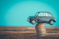 Miniature black vintage second hand car model on coins stack on wooden table. Business, finance or budget plan money saving for buying a used car and auto insurance concept. Road trip for holiday traveling.