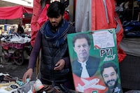 A vendor arranges shoes next to an election campaign poster of Pakistan's jailed Former Prime Imran Khan party's candidate for parliamentary election at a market, in Lahore, Pakistan, Friday, Feb. 9, 2024. The results of Pakistan's elections were delayed a day after the vote that was marred by sporadic violence, a mobile phone service shutdown and the sidelining of former Prime Minister Imran Khan and his party. (AP Photo/K.M. Chaudary)