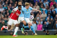 Arsenal's Thomas Partey, left, duels for the ball with Manchester City's Kevin De Bruyne during the English Premier League soccer match between Manchester City and Arsenal at the Etihad stadium in Manchester, England, Sunday, March 31, 2024. (AP Photo/Dave Thompson)