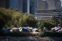 Tents and people are seen at a homeless encampment at Crab Park below the towers of the downtown skyline in Vancouver on Sunday, August 14, 2022. Residents forced out of a Vancouver homeless encampment will be allowed back in this week after the city completed a cleanup of the site. THE CANADIAN PRESS/Darryl Dyck