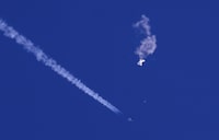 In this photo provided by Chad Fish, the remnants of a large balloon drift above the Atlantic Ocean, just off the coast of South Carolina, with a fighter jet and its contrail seen below it, Feb. 4, 2023. THE CANADIAN PRESS/Chad Fish via AP