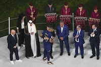FILE - Qatar Airways staff in uniform, in background, assist in the medal ceremony, as French President Emmanuel Macron hugs France's Kylian Mbappe who was awarded the Golden Boot after the World Cup final soccer match between Argentina and France at the Lusail Stadium in Lusail, Qatar, on Dec. 18, 2022. Qatar Airways will be FIFA’s airline sponsor at the men’s 2026 World Cup being played across North America. Soccer’s governing body renewed with the company through 2030 on Wednesday, Nov. 22, 2023. (AP Photo/Thanassis Stavrakis)