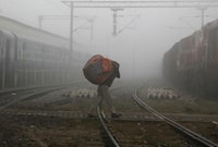 A man carries blankets as he crosses railway tracks on a foggy and cold winter morning in the northern Indian city of Allahabad December 29, 2014. REUTERS/Jitendra Prakash/File Photo