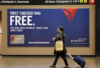 FILE - In this Tuesday, March 24, 2015, file photo, a traveler walks past a sign advertising a Delta Air Lines credit card at Seattle-Tacoma International Airport in SeaTac, Wash. Airline loyalty programs are losing much of their allure even for frequent flyers, and the rules for navigating the system have changed. The biggest bang for your buck comes from signing up for the right credit card. Even if you make purchases with another card, consider getting the card of the airline you usually fly to enjoy benefits such as priority boarding and free bag-checking, even on so-called basic economy tickets. If you check a bag a few times a year, you will more than offset the annual fee. (AP Photo/Elaine Thompson, File)