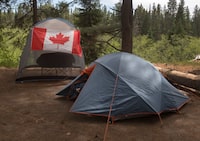 Campers with a Canadian flag flying on their camp site are shown in Algonquin Park Saturday June 12, 2021. Parks Canada says visitors will be able to start booking reservations for camping and other activities at its sites across the country in March. The reservation dates, which are posted online, are different at each national park, historic site and marine conservation area.THE CANADIAN PRESS/Fred Thornhill
