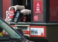 A Tim Hortons employee hands out coffee from a drive-through window to a customer in Mississauga, Ont., on Tuesday, March 17, 2020. Businesses in Vancouver will no longer be required to charge a fee for single-use cups as of May 1st, a move that reverses a decision by the previous city council. THE CANADIAN PRESS/Nathan Denette