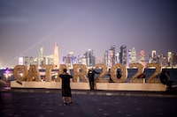 DOHA, QATAR - NOVEMBER 17: People take photos in front of a  'Qatar 2022' logo at the Corniche Waterfront Promenade with the The West Bay skyline in the back ahead of the FIFA World Cup Qatar 2022 on November 17, 2022 in Doha, Qatar. (Photo by Matthias Hangst/Getty Images)
